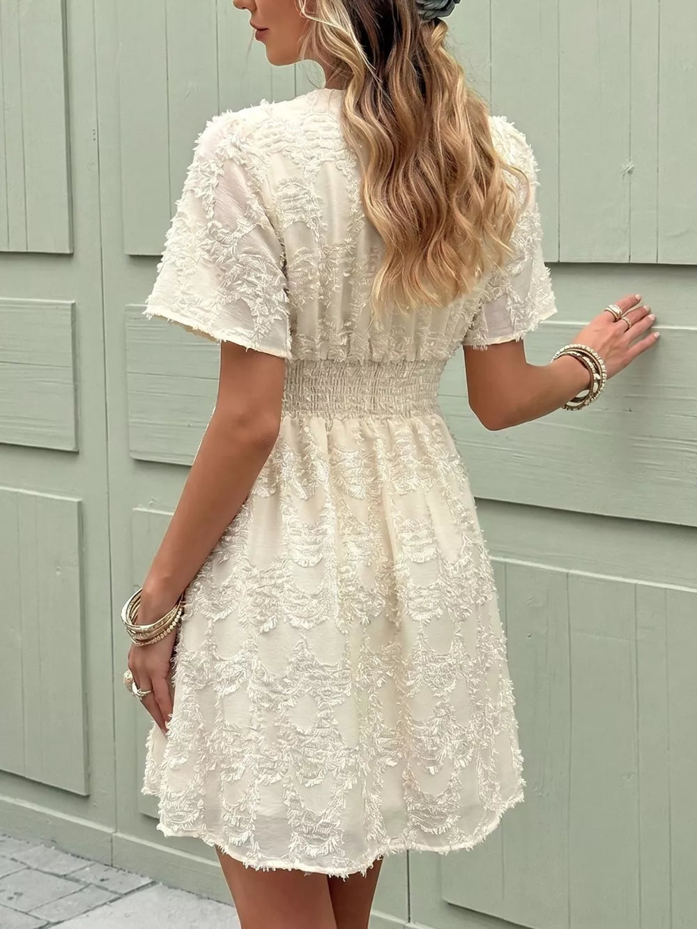 Chic textured mini dress in apricot with a deep V-neck and ruched waist detail.