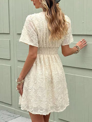 Chic textured mini dress in apricot with a deep V-neck and ruched waist detail.