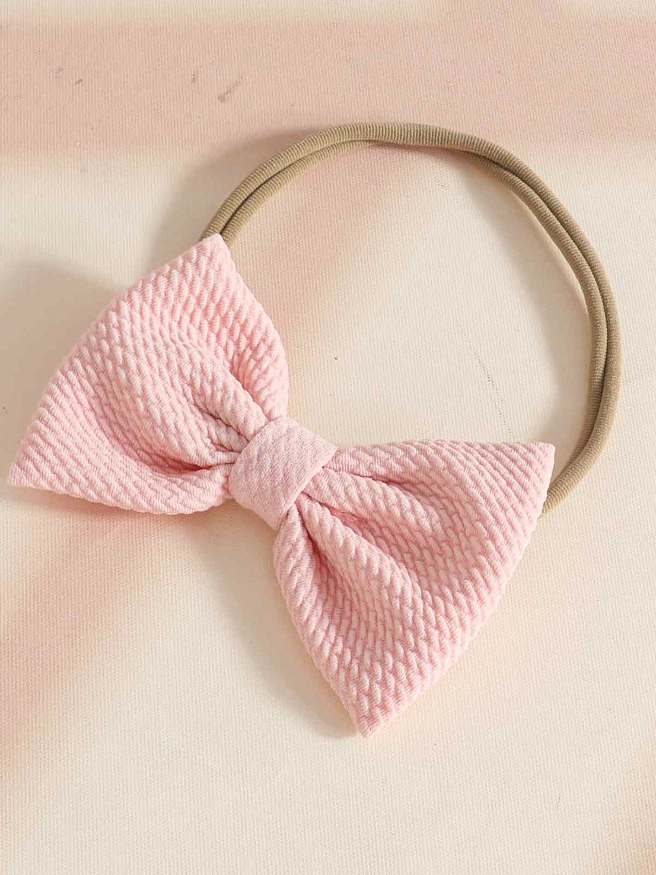 Pink textured bow headband with a tan elastic band.