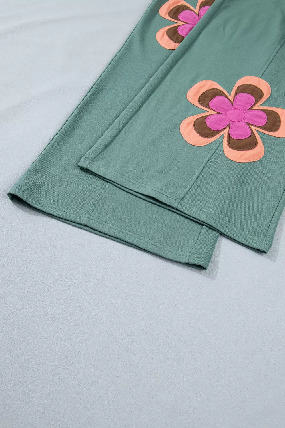 Green cotton sweatpants with floral appliques and drawstring detail.