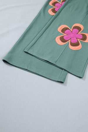 Green cotton sweatpants with floral appliques and drawstring detail.