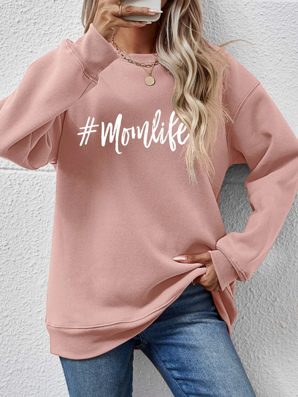 Blush pink crewneck sweatshirt with white #Momlife graphic, long sleeves, and casual fit.