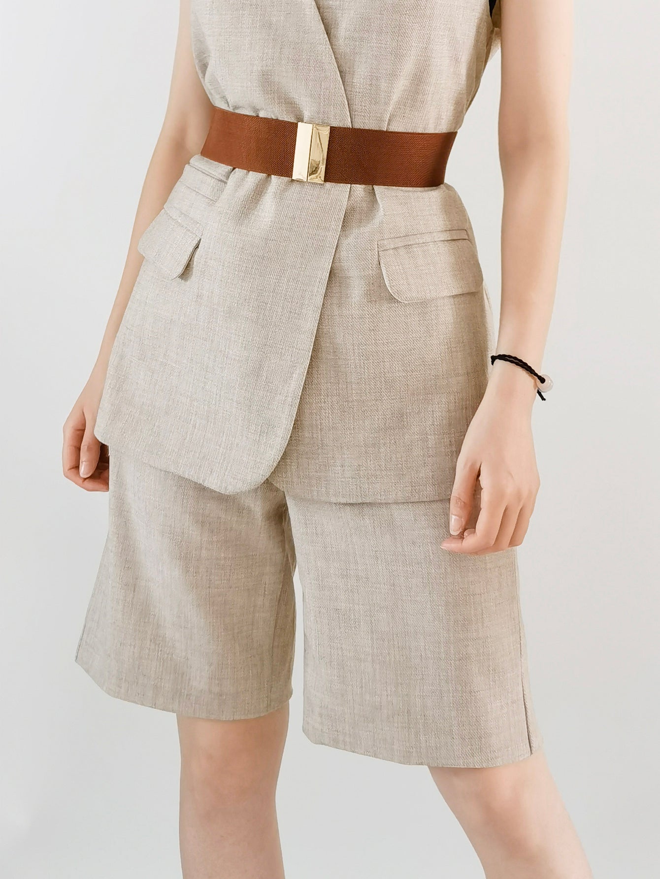 Wide elastic belt in tan with a gold clasp, cinching a linen blend vest and shorts.