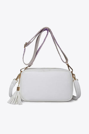 White textured crossbody bag with tassel detail and purple-accented strap