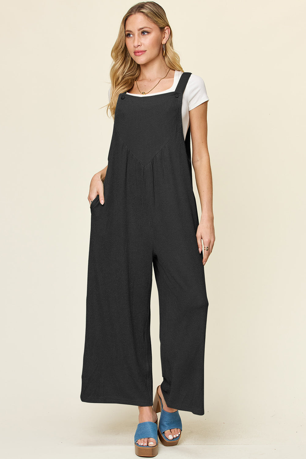 Black ribbed wide-leg pinafore jumpsuit with button straps and pockets.
