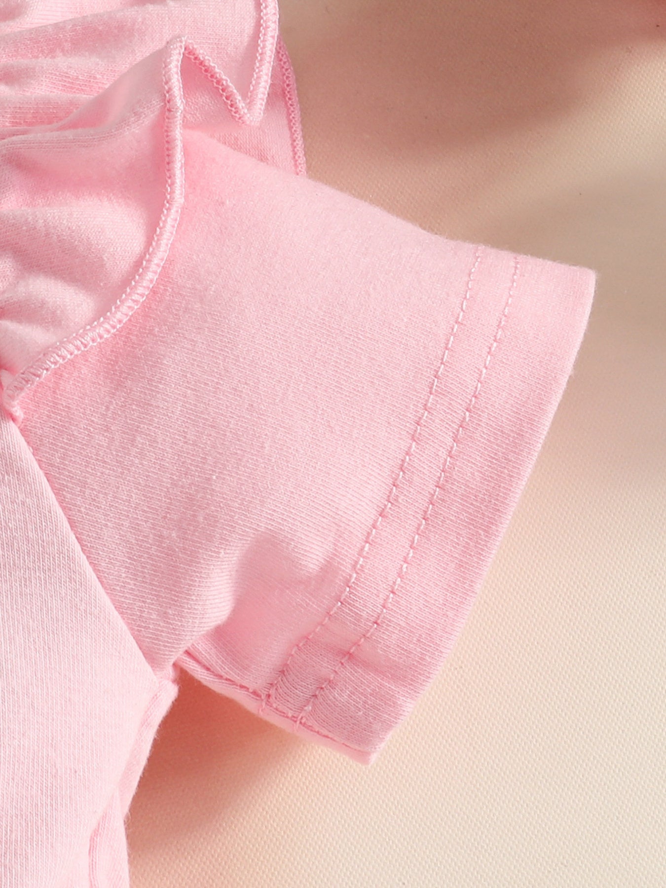 Pink baby dress with ruffled neckline detail and short sleeves.