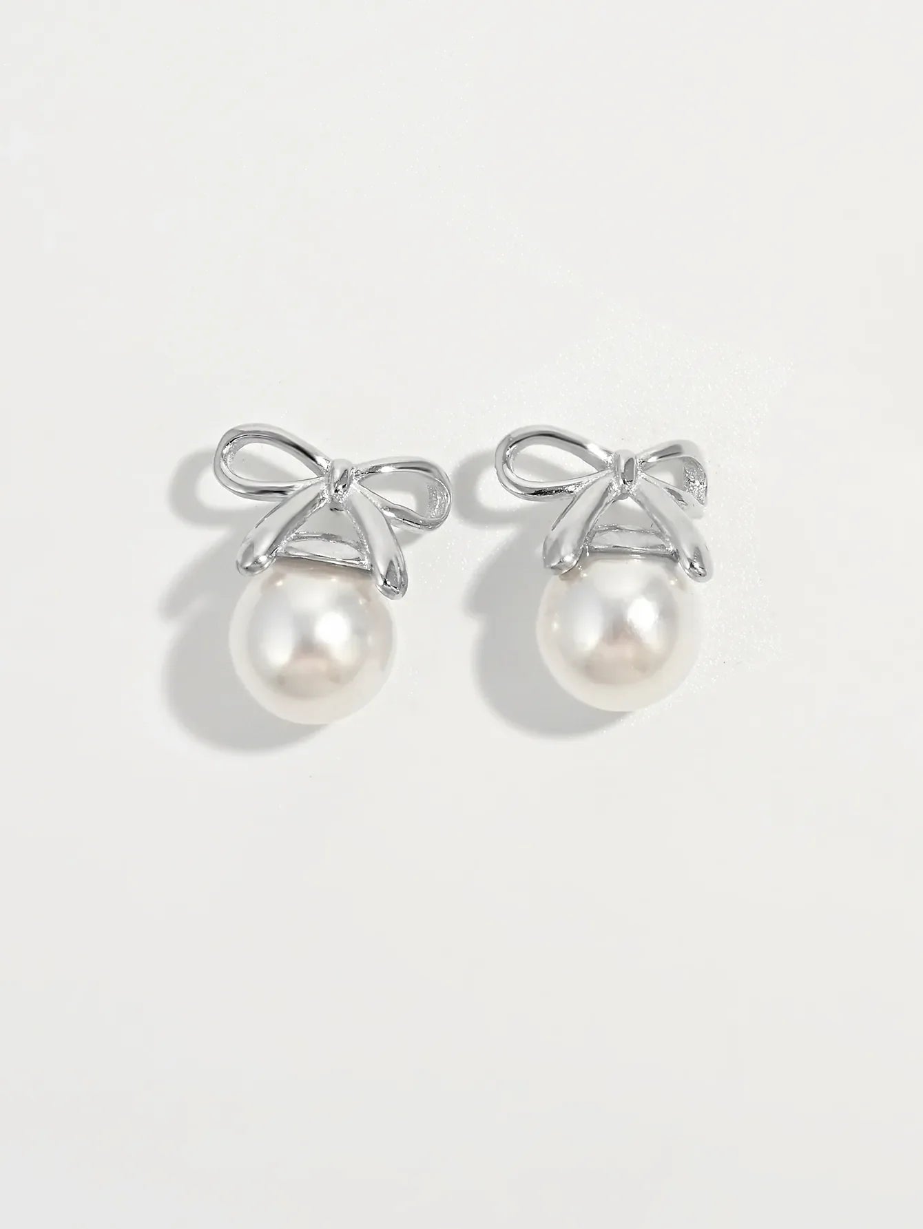 Silver bow pearl drop earrings with white pearls on a white background.