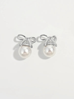 Silver bow pearl drop earrings with white pearls on a white background.