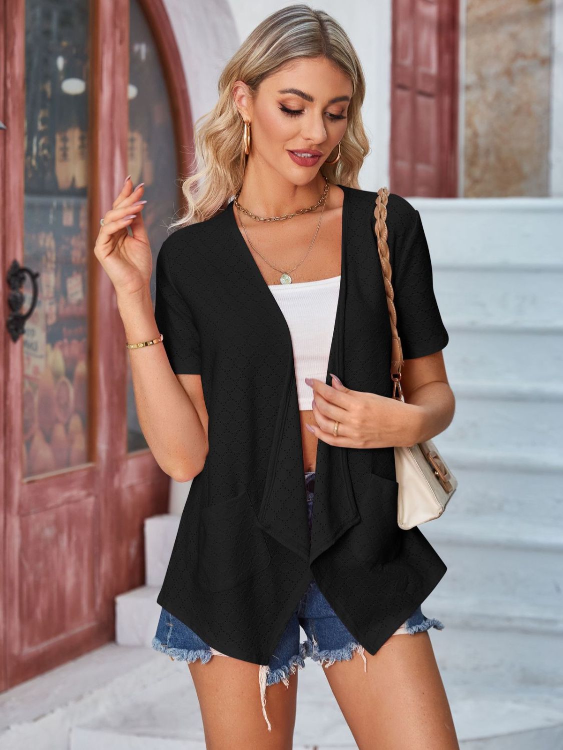 Black perforated shawl collar jacket with short sleeves and open front, styled with a white crop top and denim shorts.