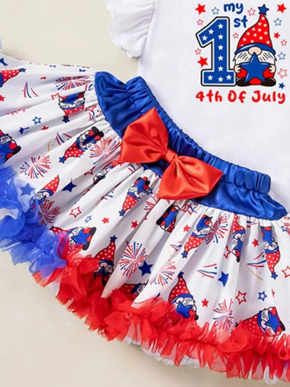 Baby girl's festive outfit with gnome print skirt, red bow, and ruffled trim.