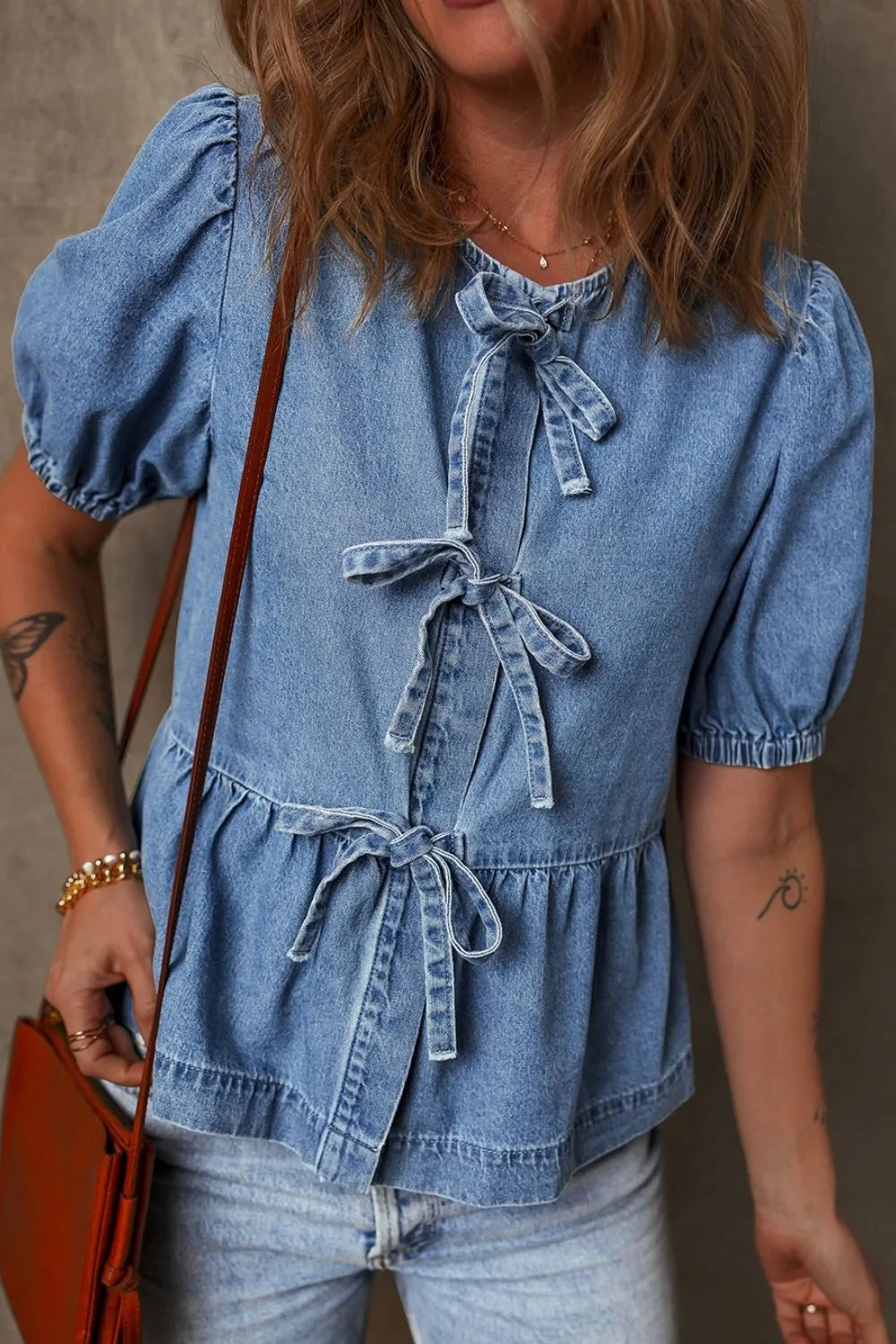 Denim peplum blouse in medium wash with puff sleeves and multiple front bow ties.
