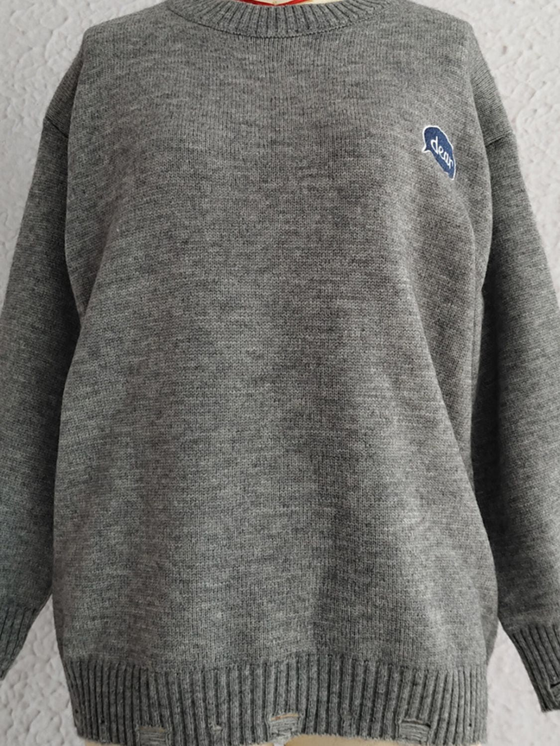 Dark gray acrylic knit sweater with embroidered blue oval detail and distressed hem.