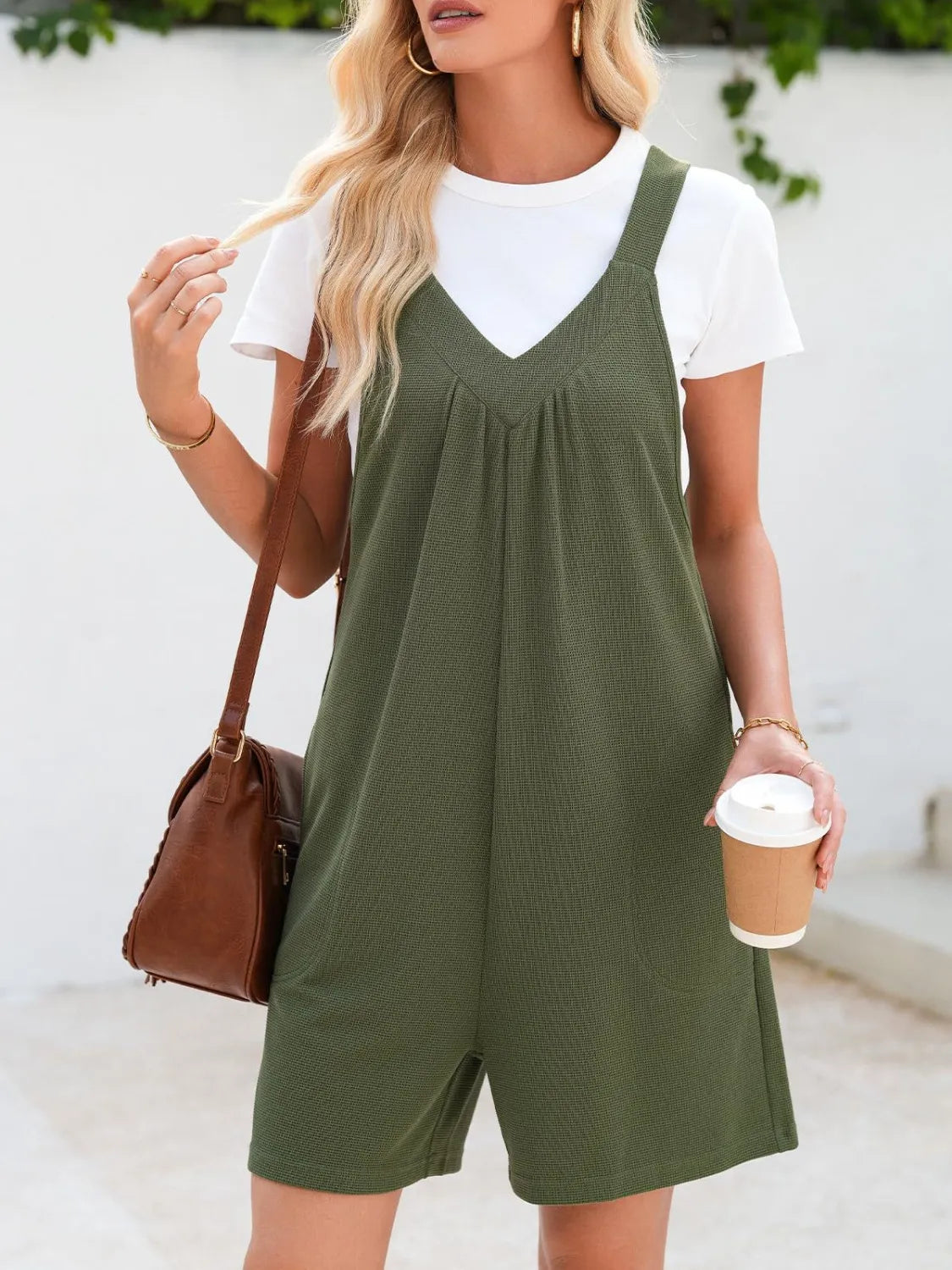 Moss green textured romper with gathered yoke and v-neck, styled with a white tee and brown crossbody bag.