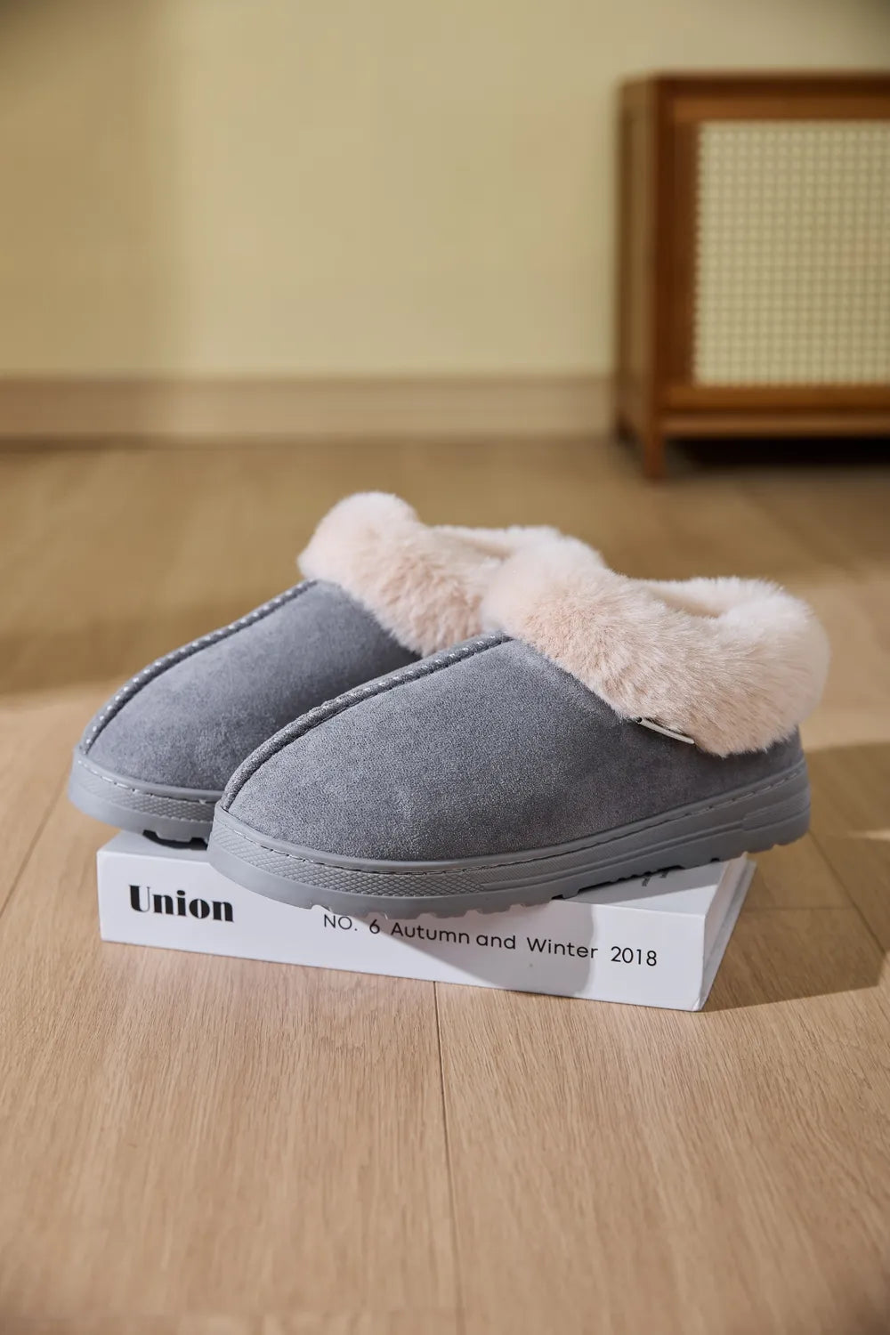 Gray suede house slippers with plush shearling trim and decorative stitching.