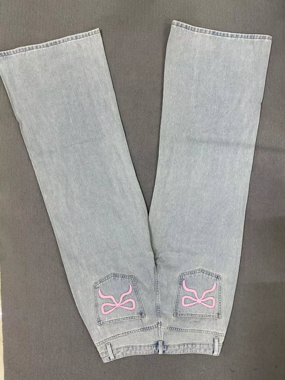 Light wash denim jeans with relaxed fit and pink embroidered back pockets.