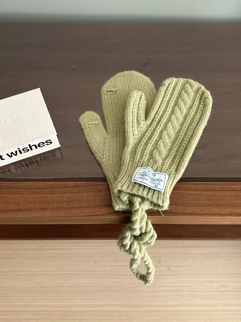 Green cable knit acrylic gloves with a braided pattern and attached rope detail.