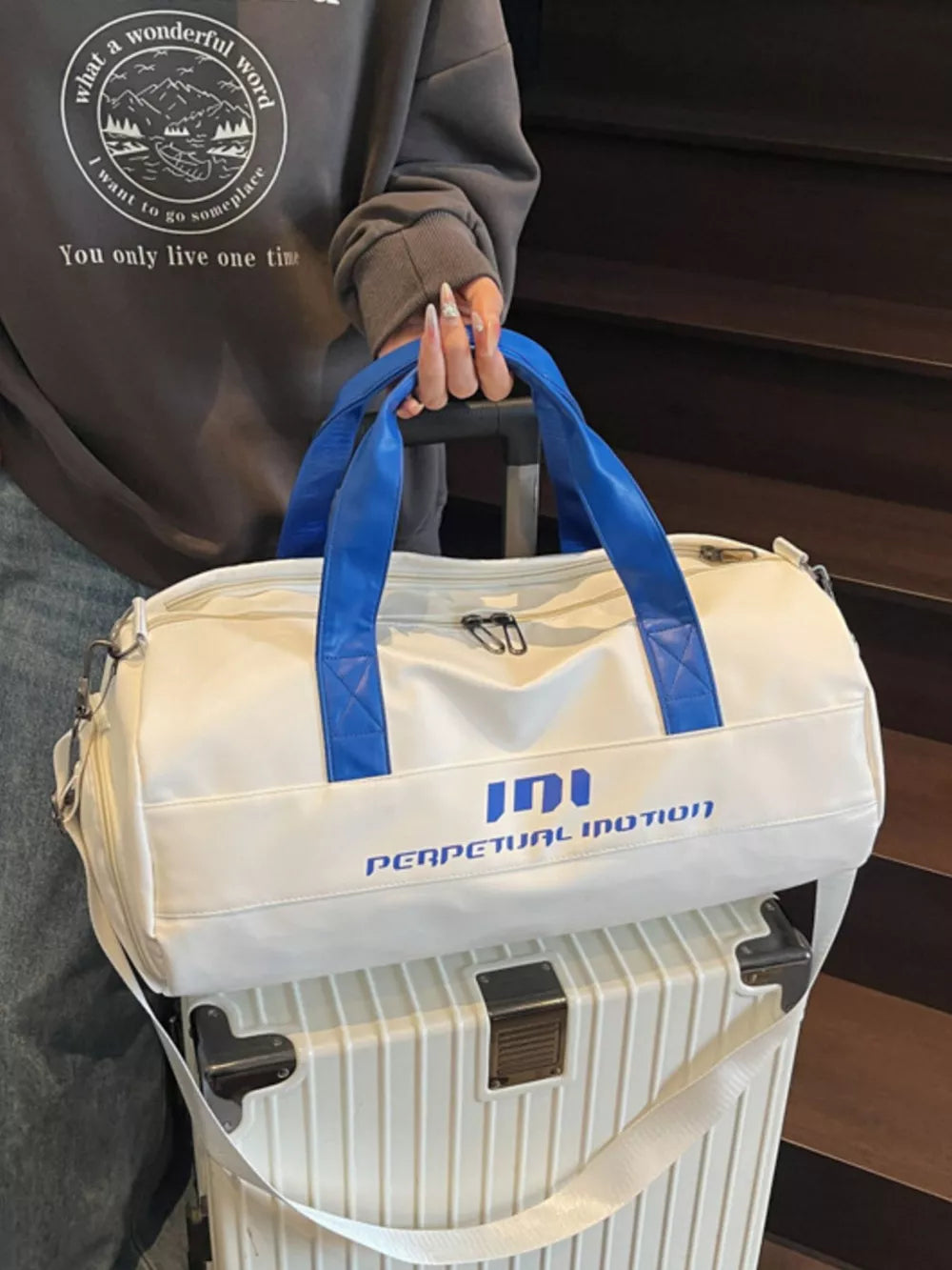 Off-white duffel bag with blue handles and "PERPETUAL MOTION" graphic, pu leather.