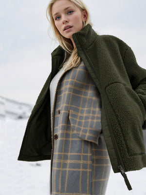 Olive green sherpa jacket with stand collar and zipper detail, worn over a plaid vest.