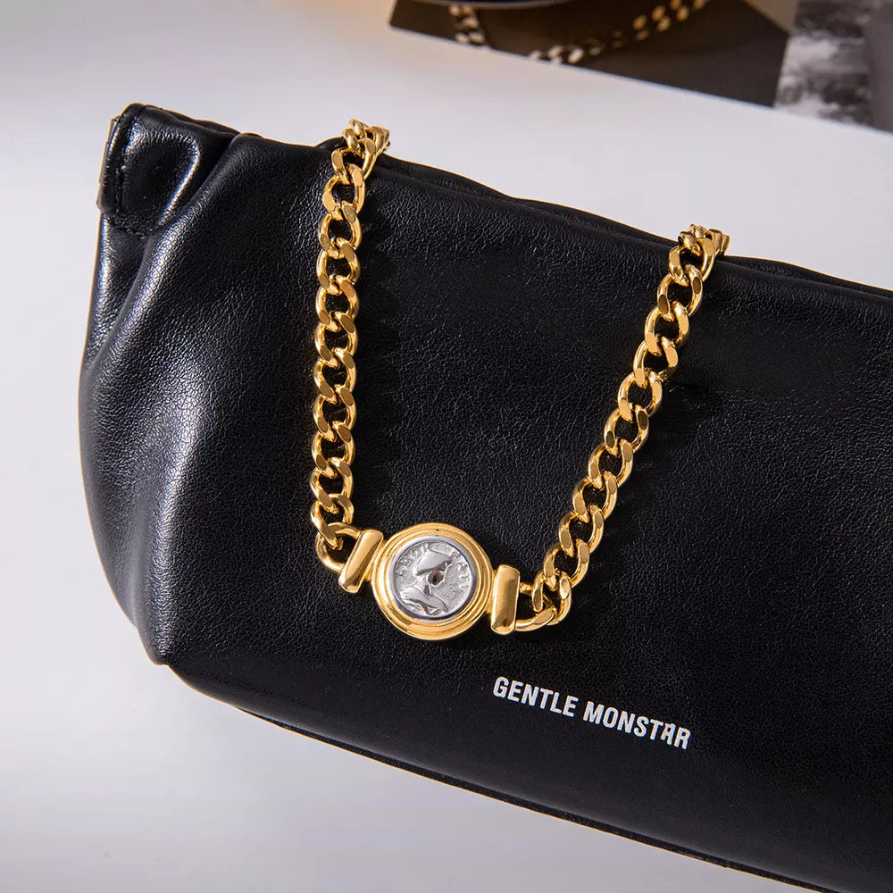 Gold curb chain necklace with vintage coin charm detail on black leather.