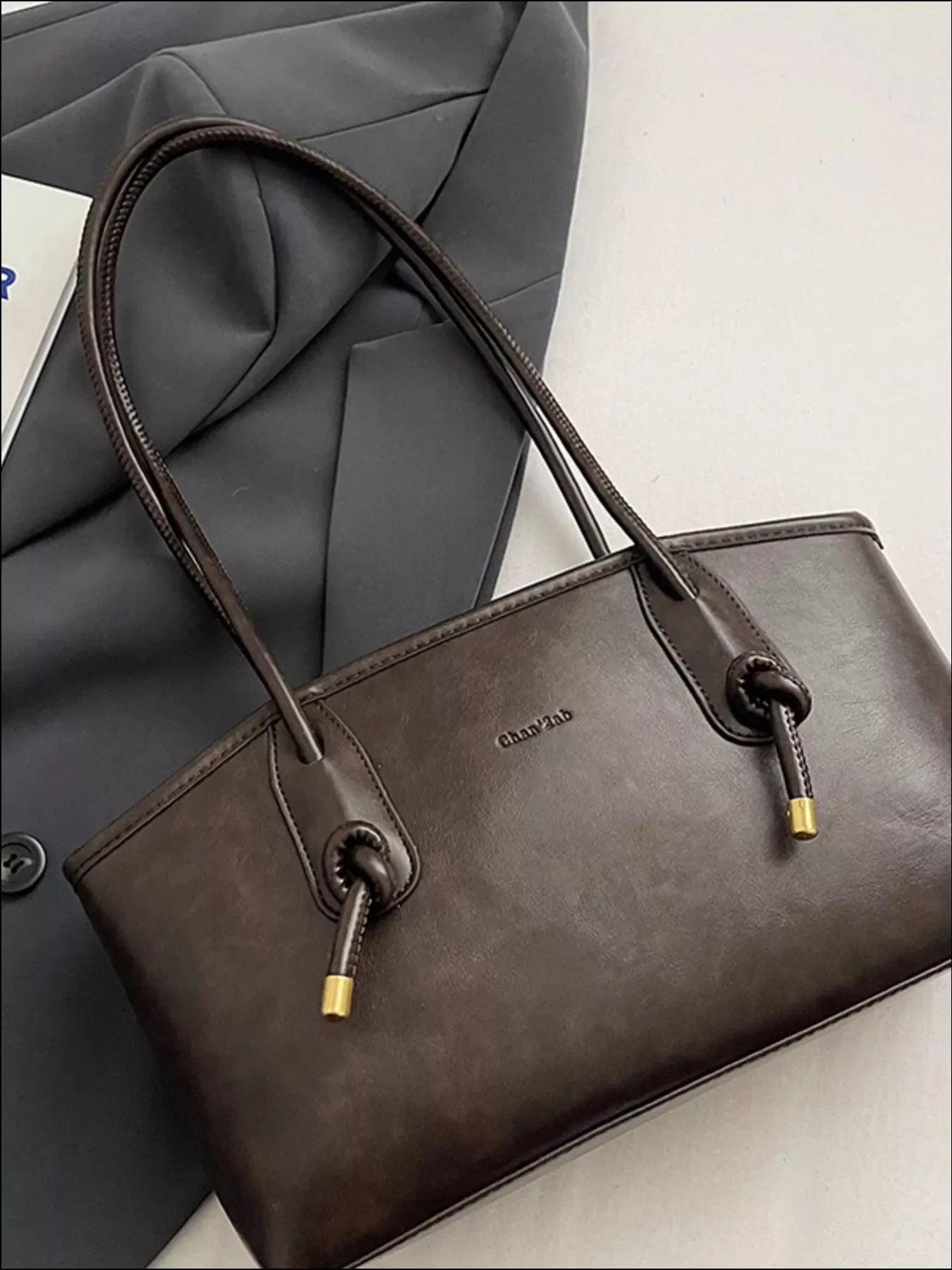 Brown leather shoulder bag with knotted strap details and gold accents.