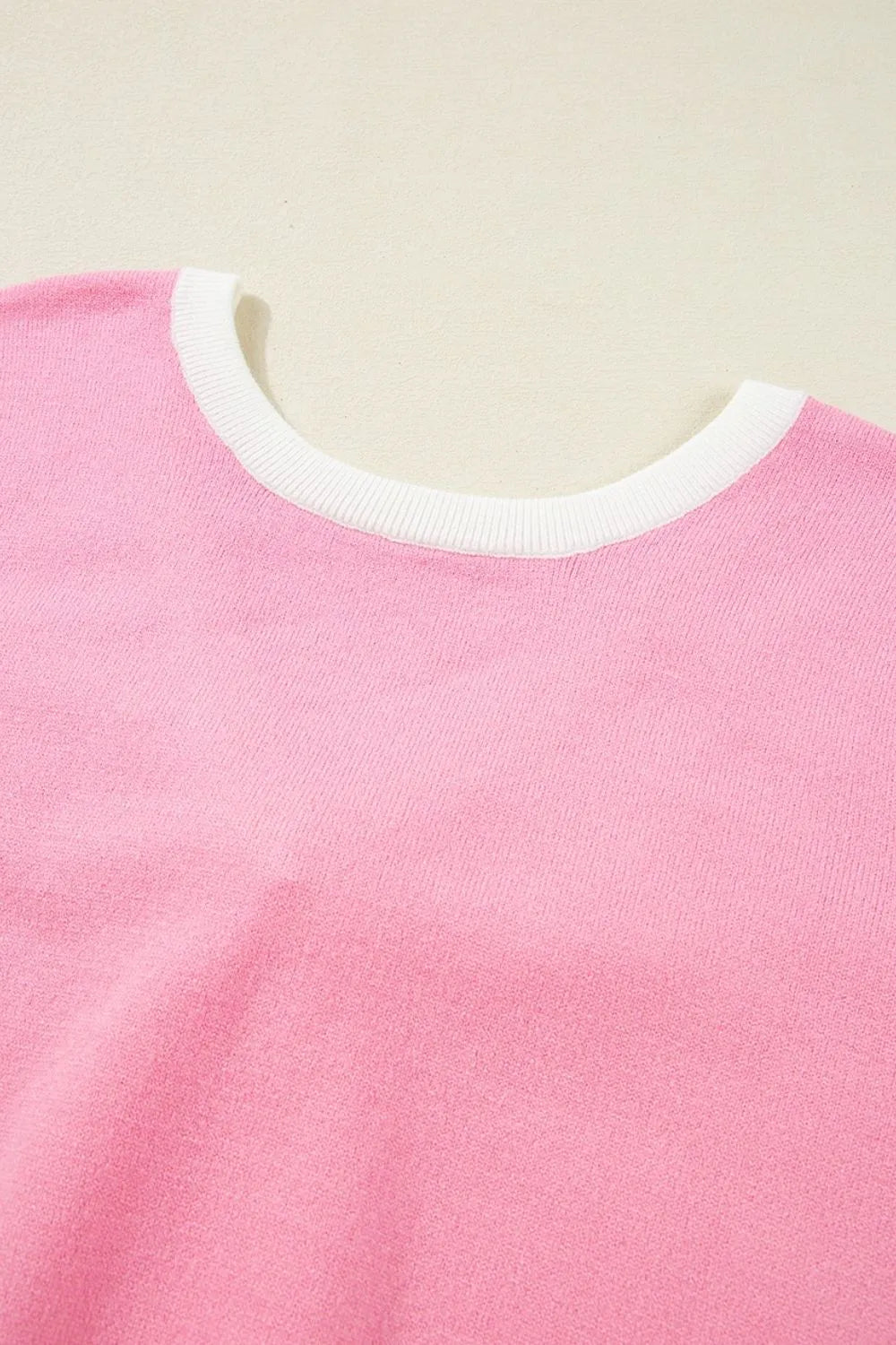 Pink knit blouse with white contrast trim neckline and back bow detail.