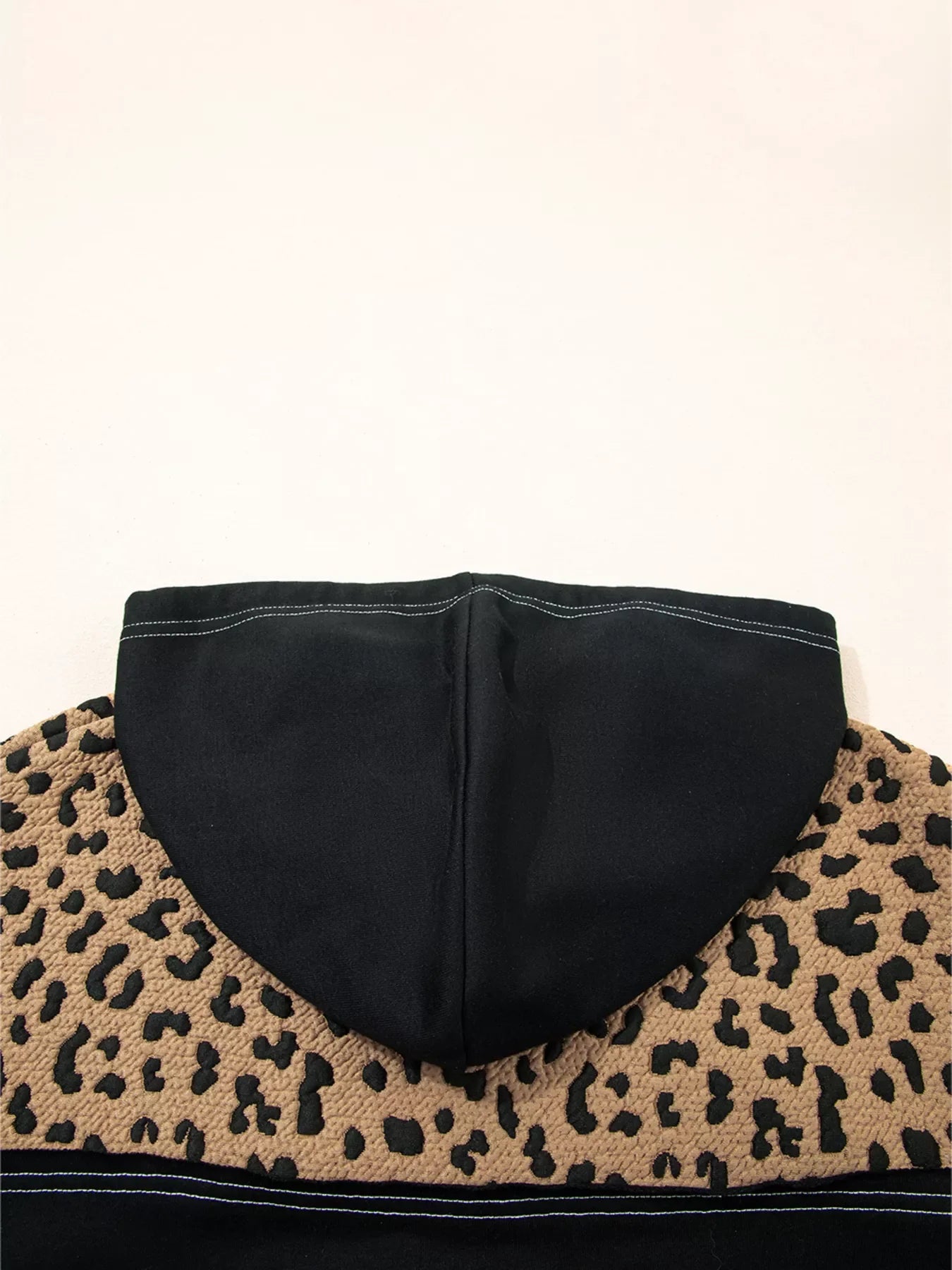 Leopard print hoodie with black hood and textured fabric detail.