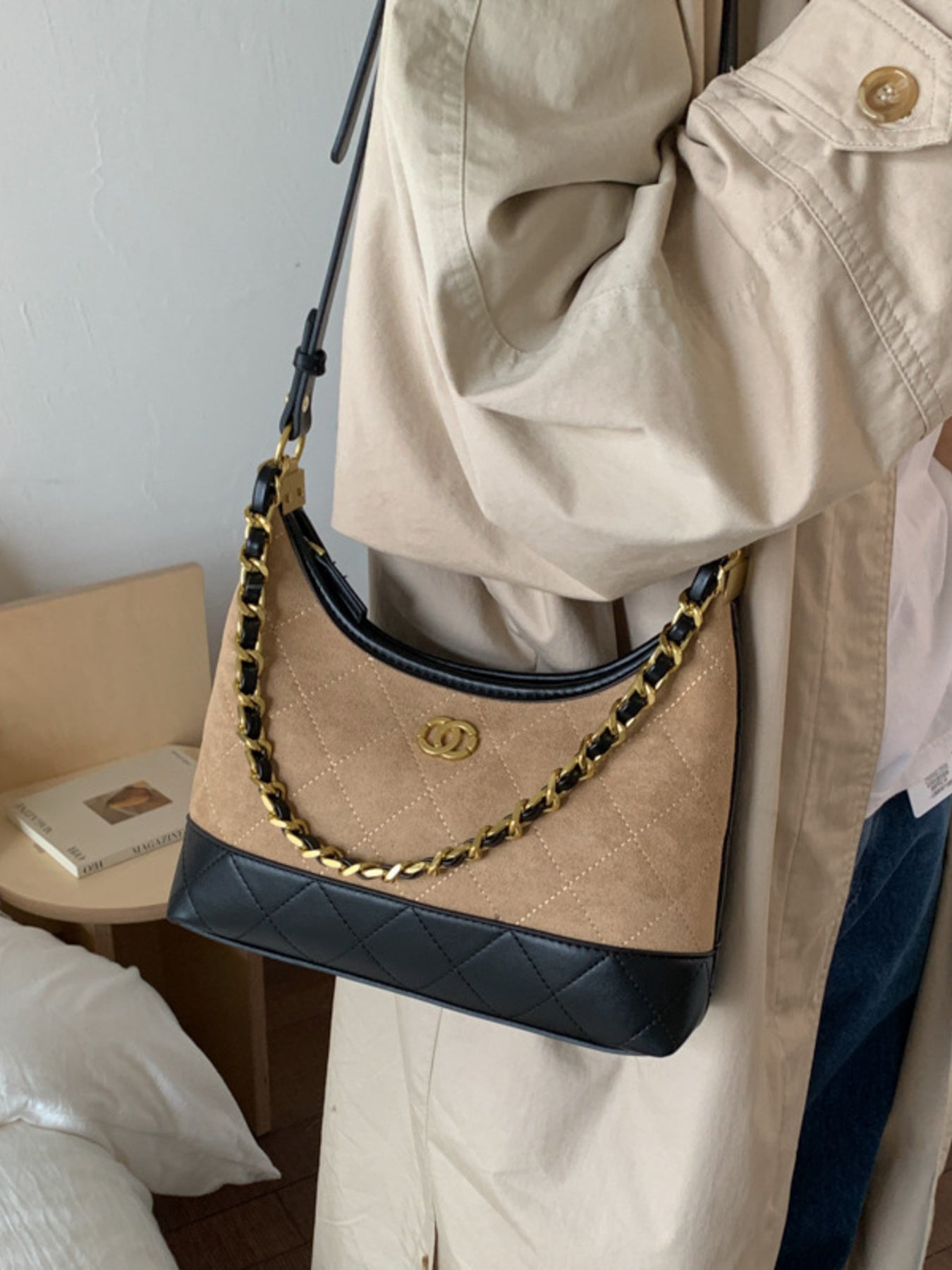 Half-moon crossbody bag in tan suede with black quilted trim and gold chain strap.