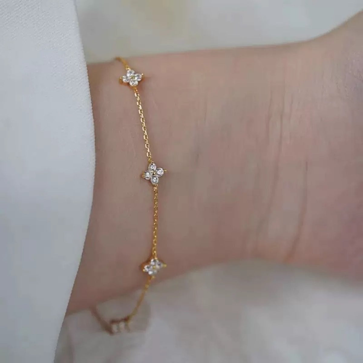 Gold delicate bracelet with four-leaf clover charms and sparkling stones.