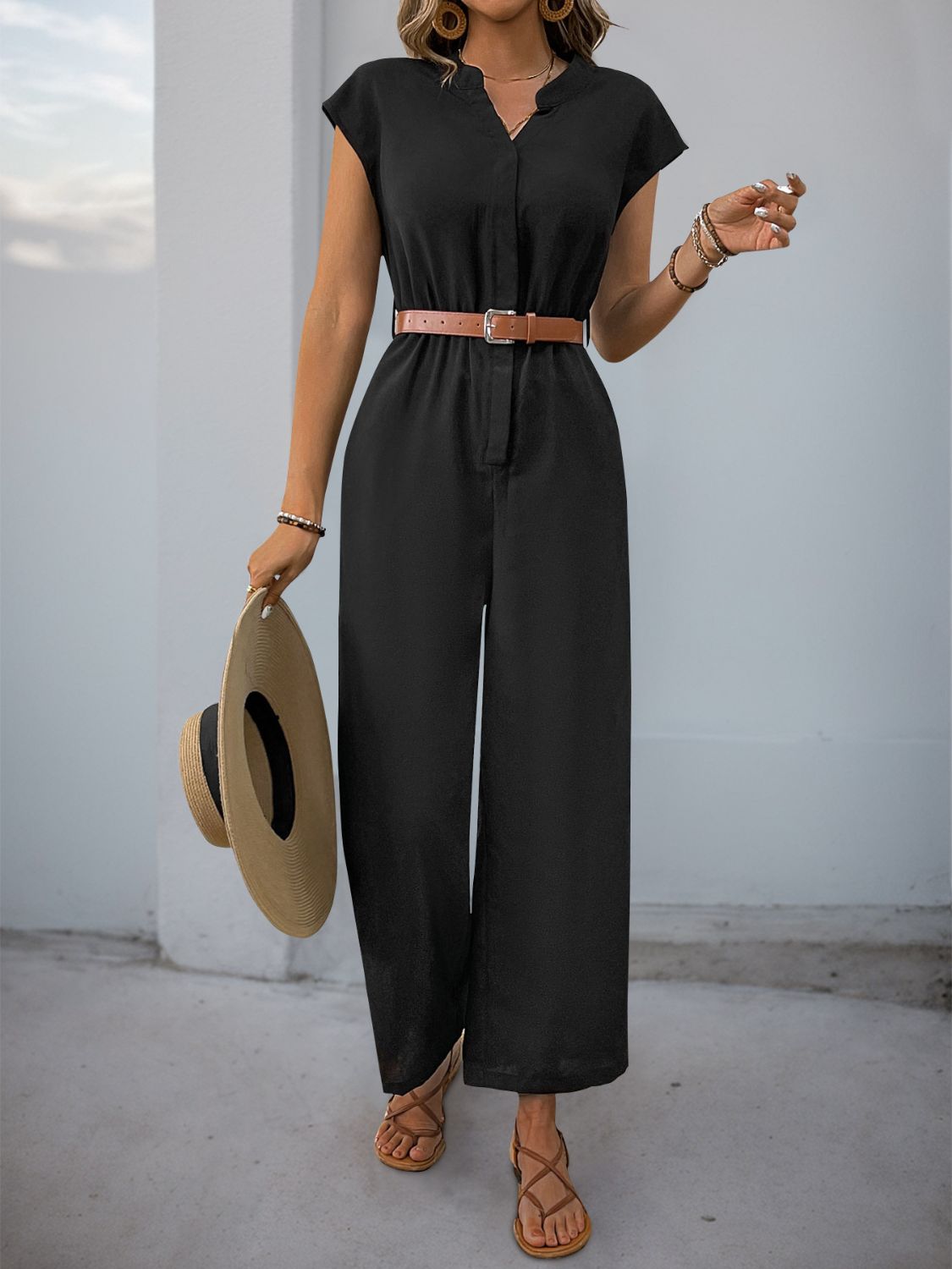 Black cap-sleeve button-down wide-leg jumpsuit with a brown belt and straw hat.