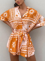 Celestial print wrap romper in orange with sun and moon pattern, short sleeves, and tie waist.