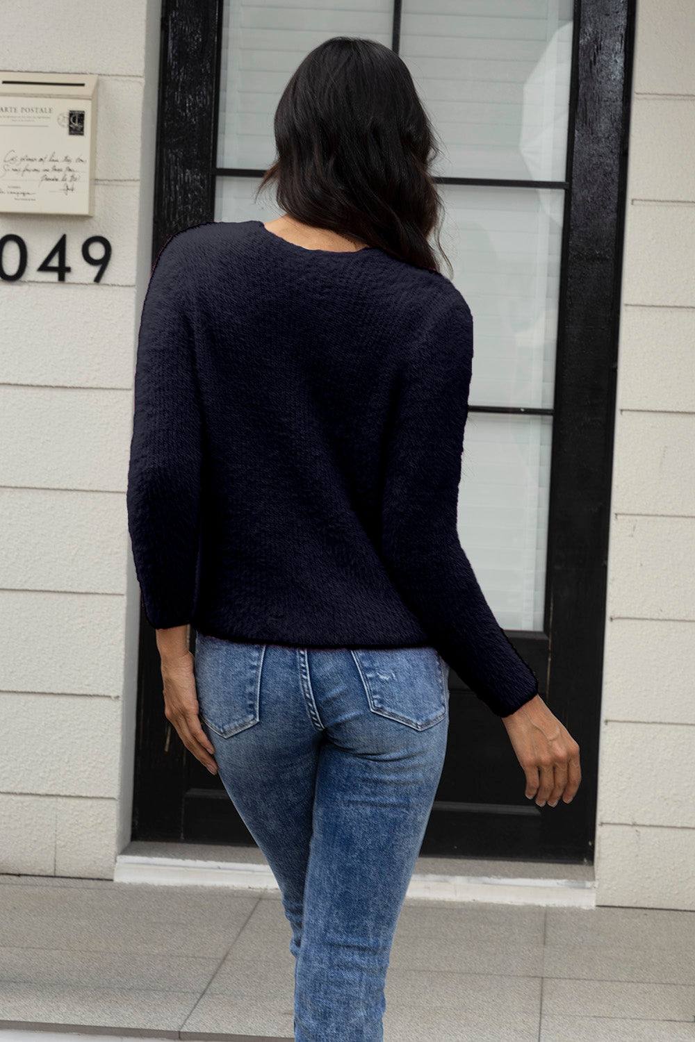 Black fluffy knit cardigan with crew neck and long sleeves, worn with denim jeans.