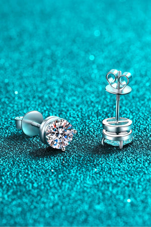 Moissanite solitaire stud earrings with rhodium finish on a sparkly teal background.