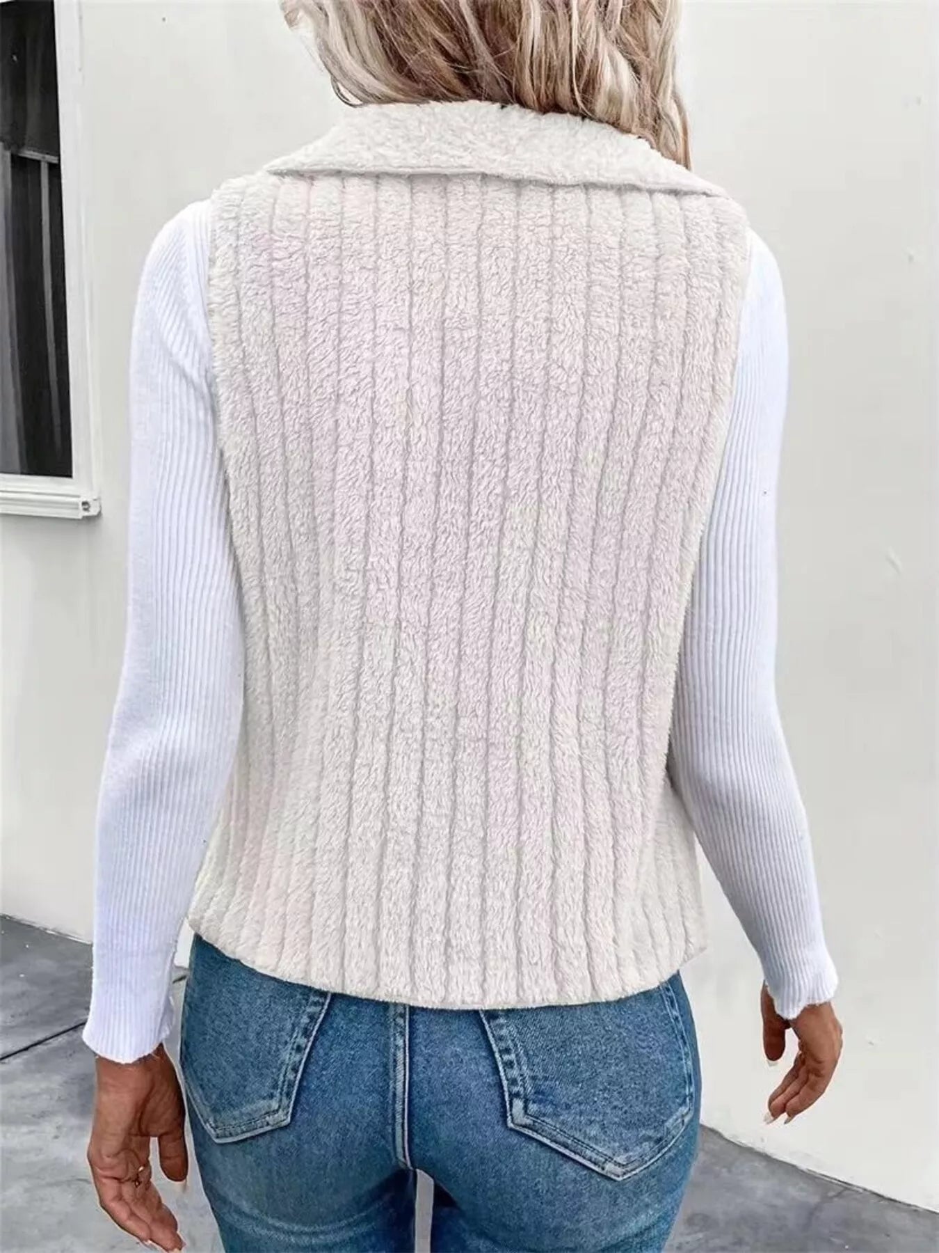 White fleece vest with vertical ribbing and a collared neckline, worn over a white long-sleeve shirt.