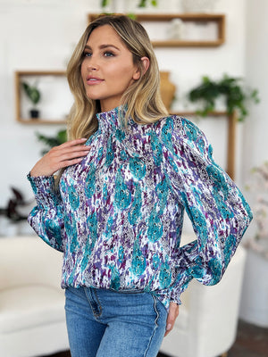 High neck abstract print blouse with smocked cuffs and neckline in blue and red-violet.