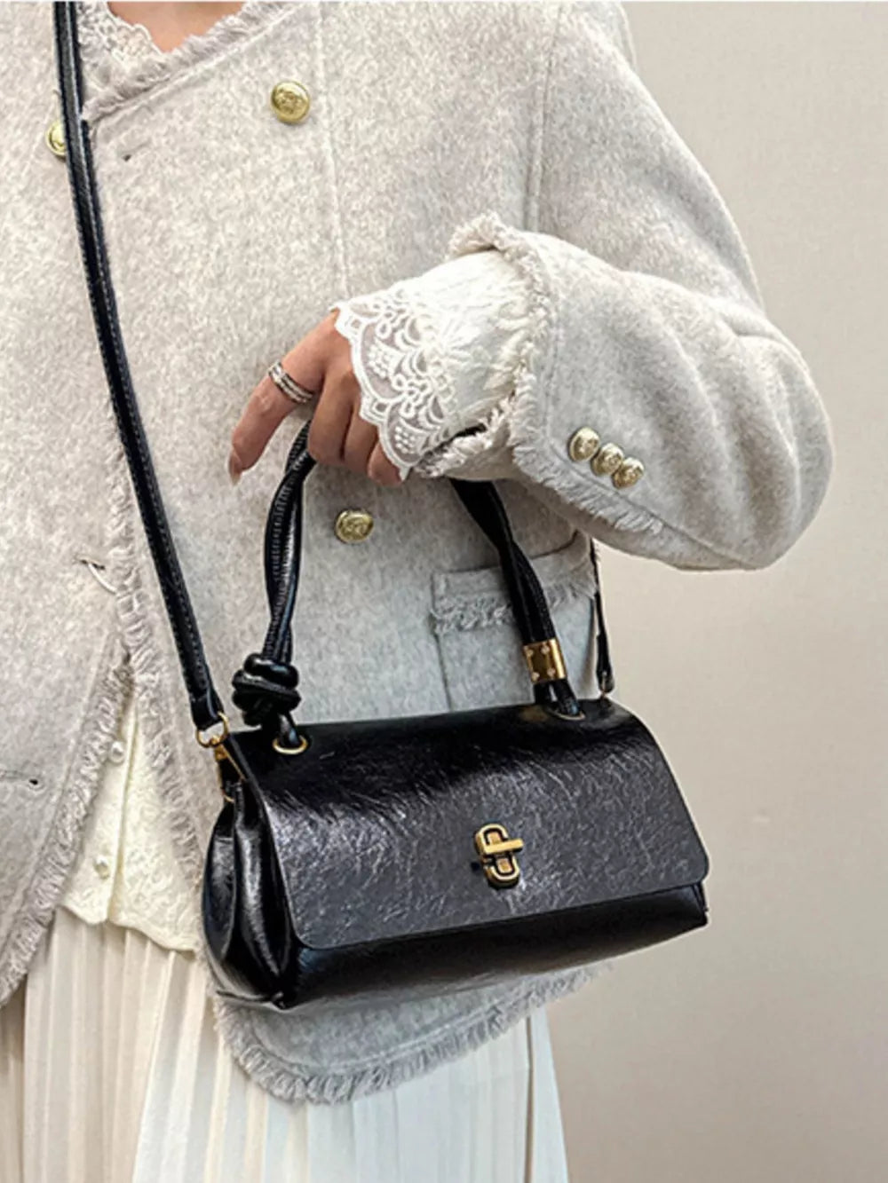 Black patent leather crossbody bag with twisted handle and gold clasp