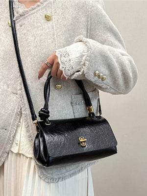 Black patent leather crossbody bag with twisted handle and gold clasp