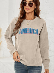 Sand corduroy sweatshirt with "AMERICA" graphic in red, white, and blue stars and stripes.