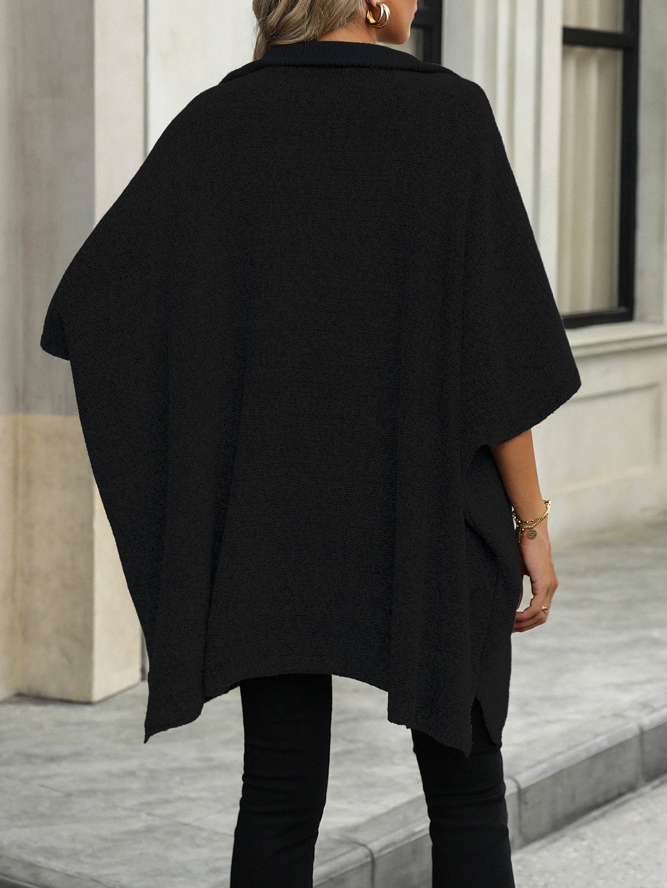 Black knit asymmetrical zip-neck poncho with short sleeves and side slits.