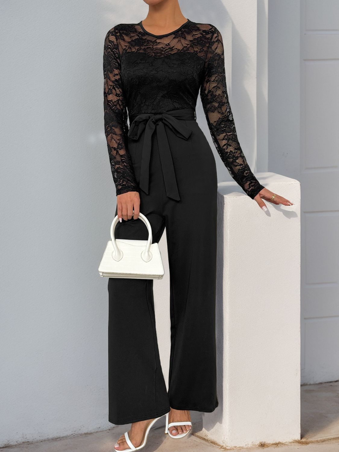 Black lace bodice wide-leg jumpsuit with tie waist and long sleeves.