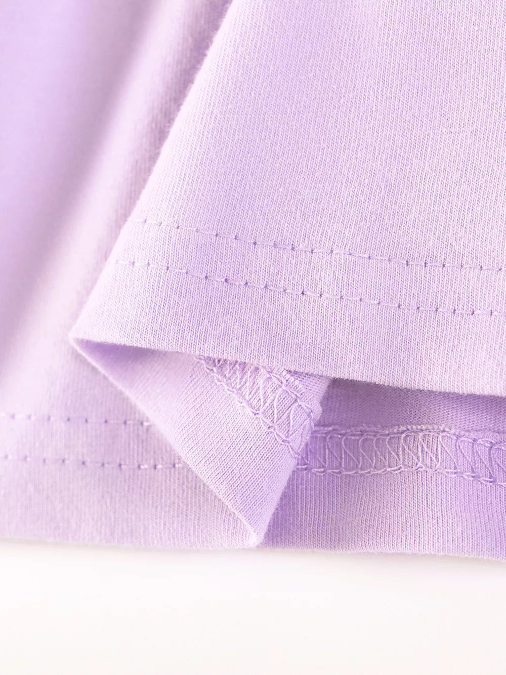 Lavender cotton baby dress hem detail with ruffled edge and stitching.