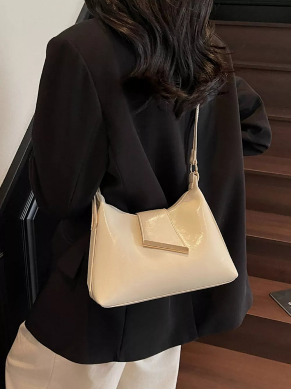 Beige patent leather crossbody bag with gold hardware detail.