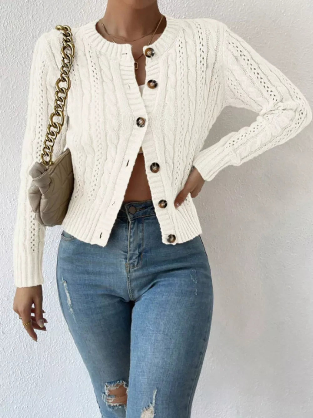 White cable-knit button-front cardigan with round neckline and brown buttons.