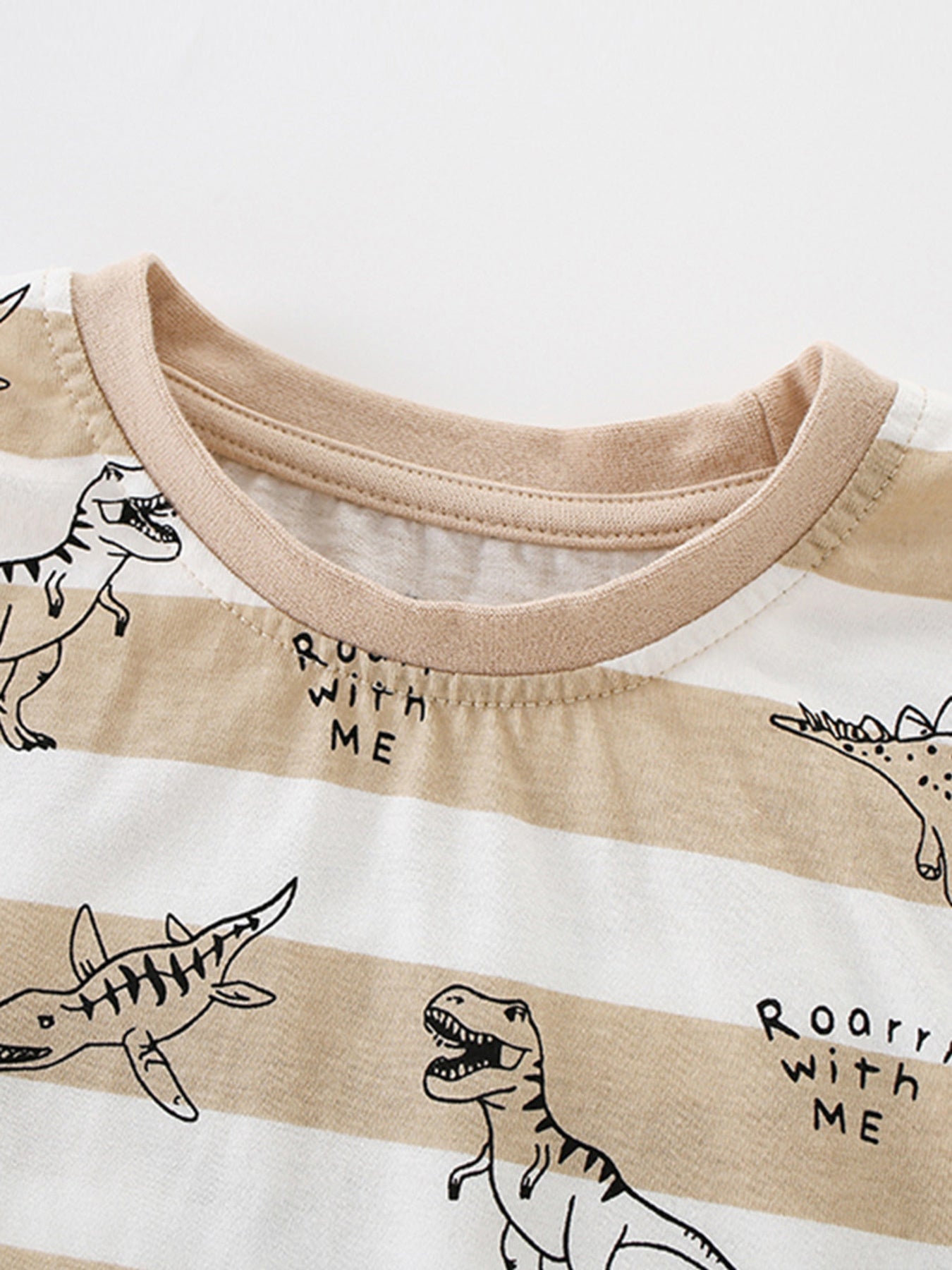 Toddler t-shirt with beige and white stripes, dinosaur print, and text detail.
