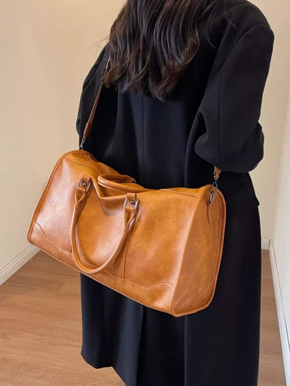 Cognac vintage leather duffle bag with top handles and shoulder strap.