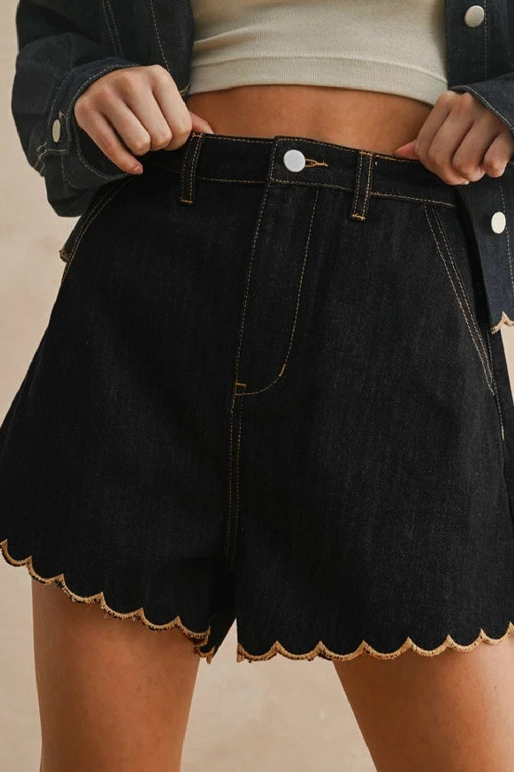 Black denim shorts with scalloped hem and contrast stitching.