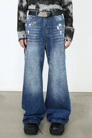 Painterly denim palazzo trousers in medium wash with artistic paint splatters and wide leg.