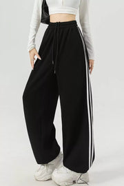 Black athletic-inspired wide-leg sweatpants with drawstring and white side stripes.