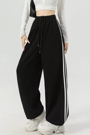 Black athletic-inspired wide-leg sweatpants with drawstring and white side stripes.