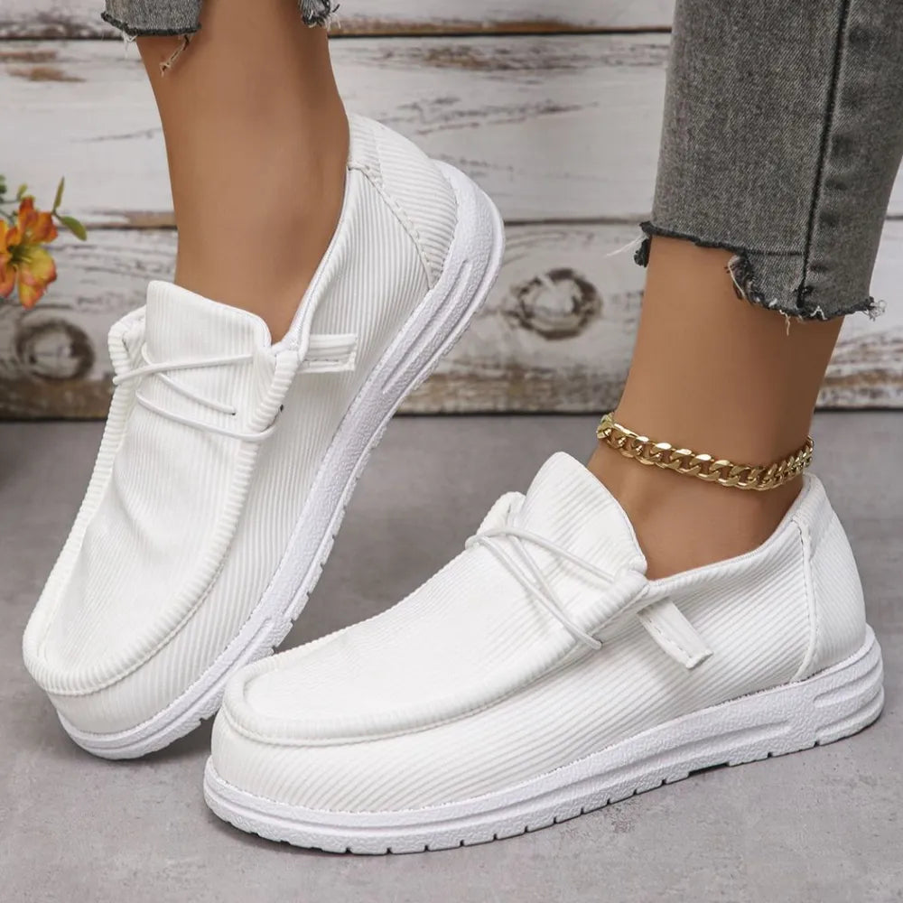 White textured slip-on espadrille sneakers with white laces and a gold chain anklet.