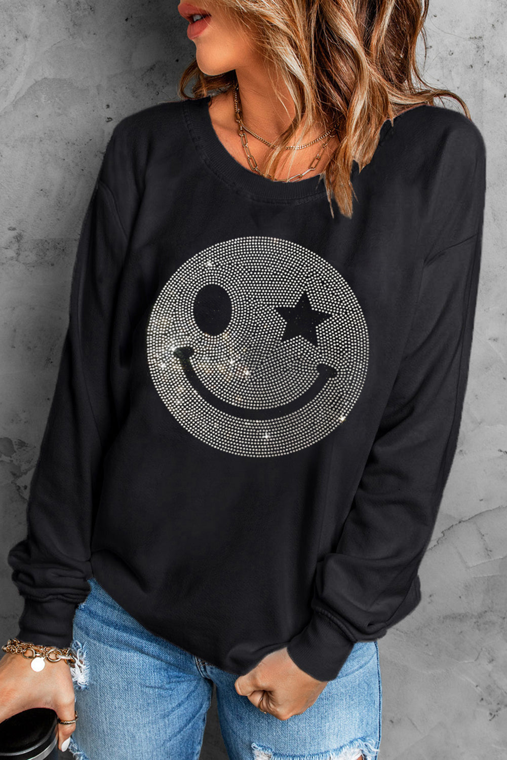 Black crewneck sweatshirt with a rhinestone wink-star smiley face graphic.